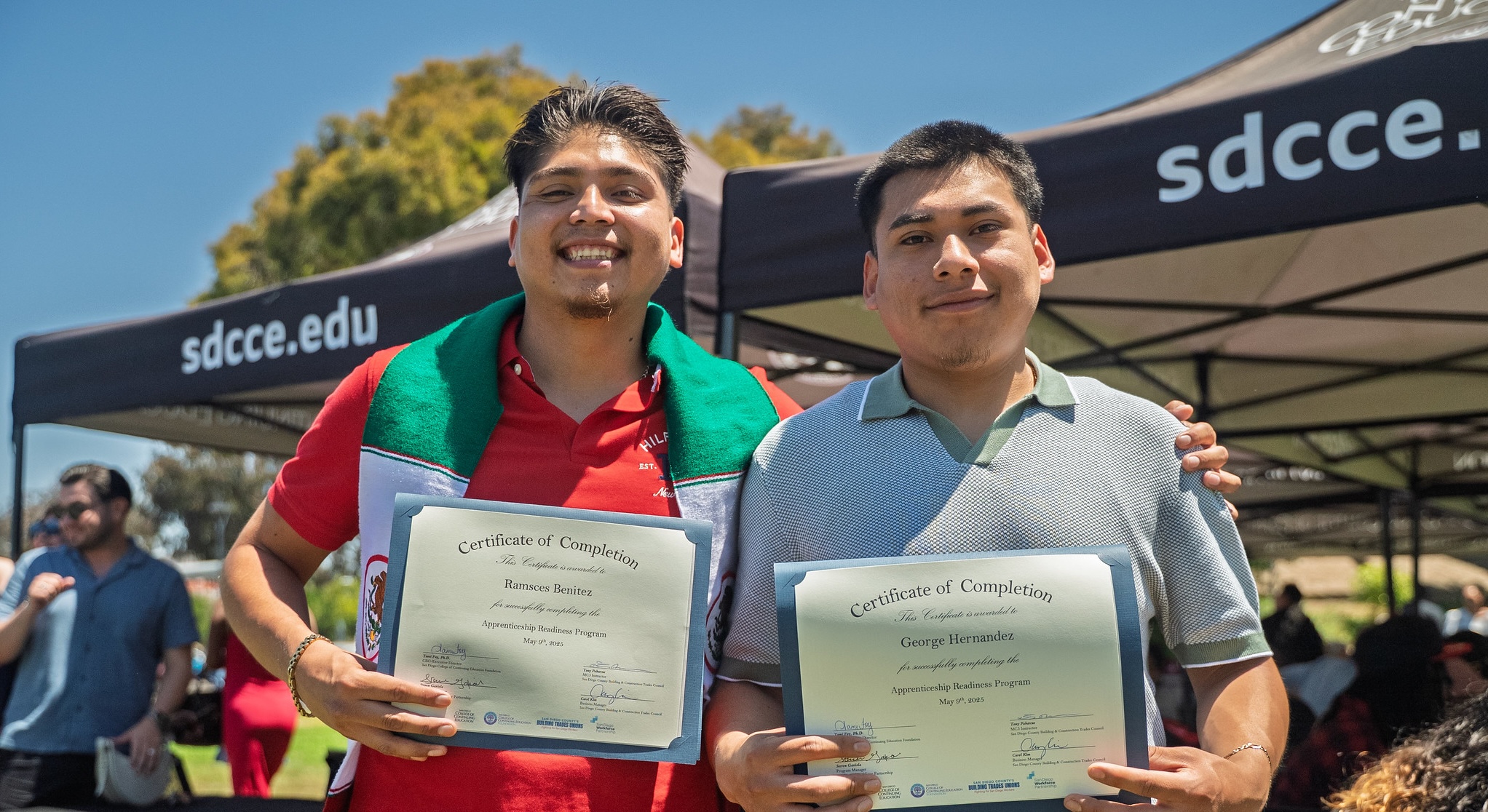 Two male students holding their certificates outside. 